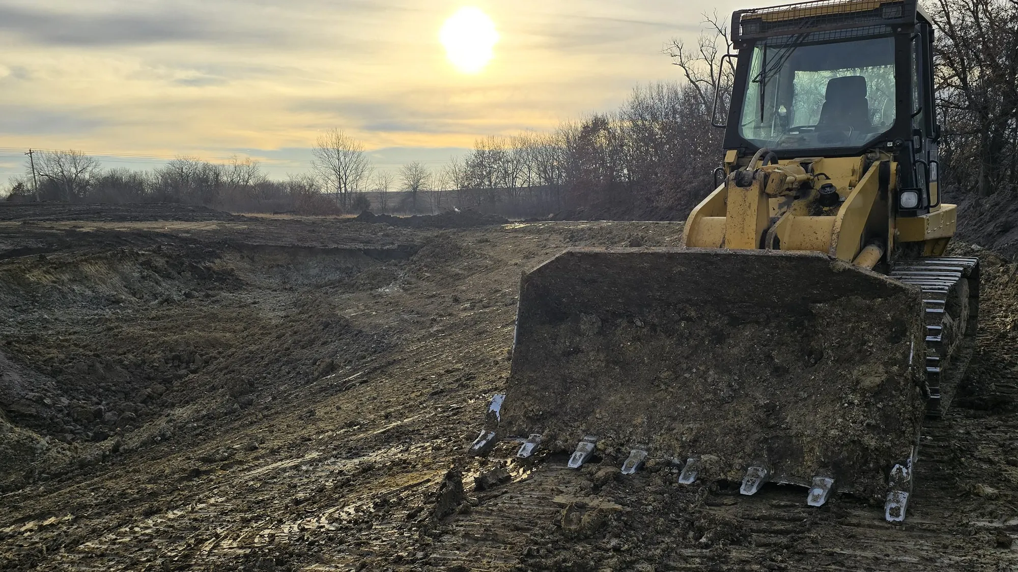 A track loader grading a jobsite at golden hour